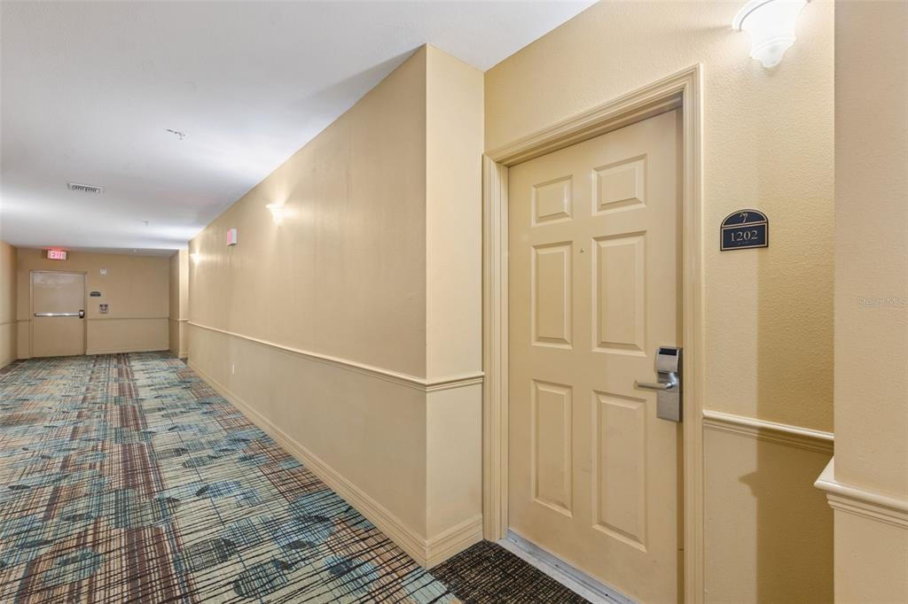 A hallway with patterned carpet leads to a door labeled 1202 in a beige building — 8112 POINCIANA BOULEVARD UNIT 1202, ORLANDO, FL