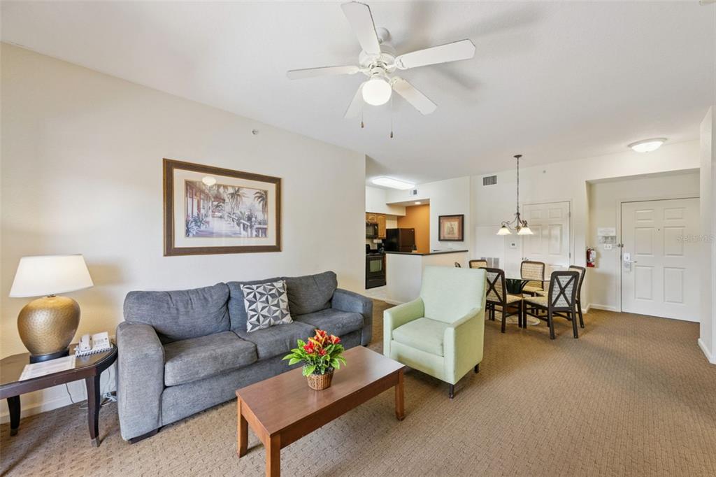 A living room with a gray sofa, a light green armchair, and a dining area — 8112 POINCIANA BOULEVARD UNIT 1202, ORLANDO, FL