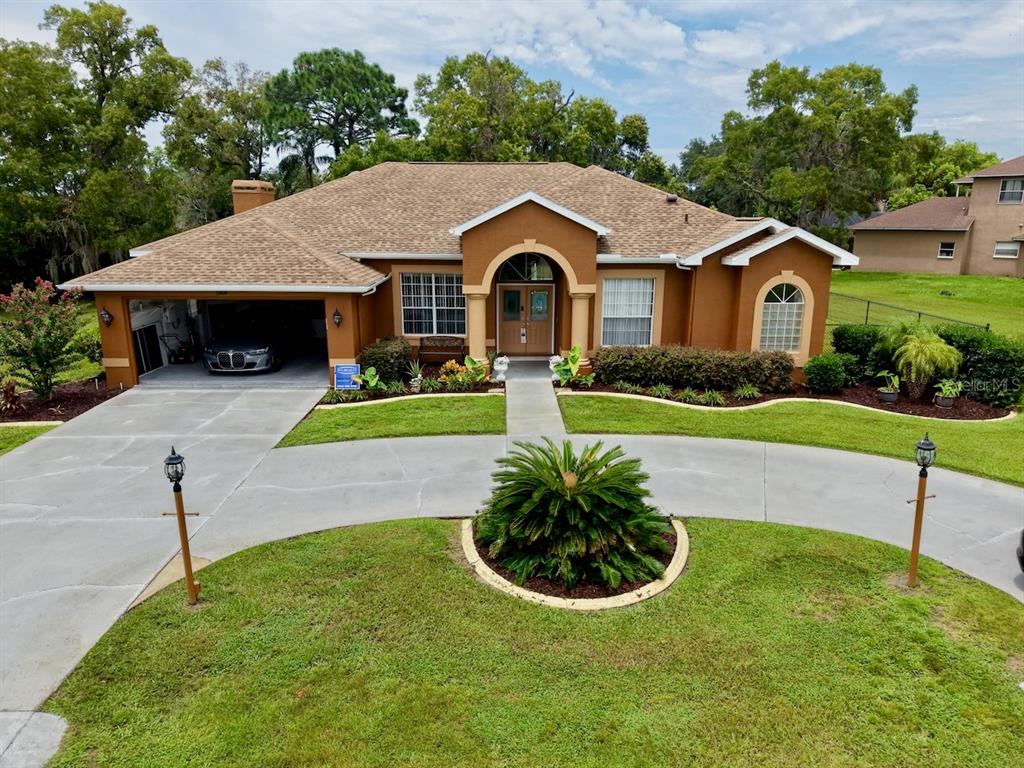 A single-story house with a brown stucco exterior, a two-car garage, and a circular driveway — 13808 RUDI LOOP, SPRING HILL, FL