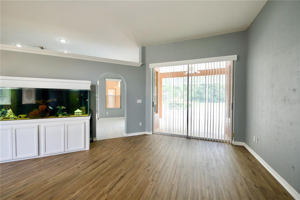 A living room features wood-look flooring, gray walls, a large fish tank, and sliding glass doors — 13808 RUDI LOOP, SPRING HILL, FL