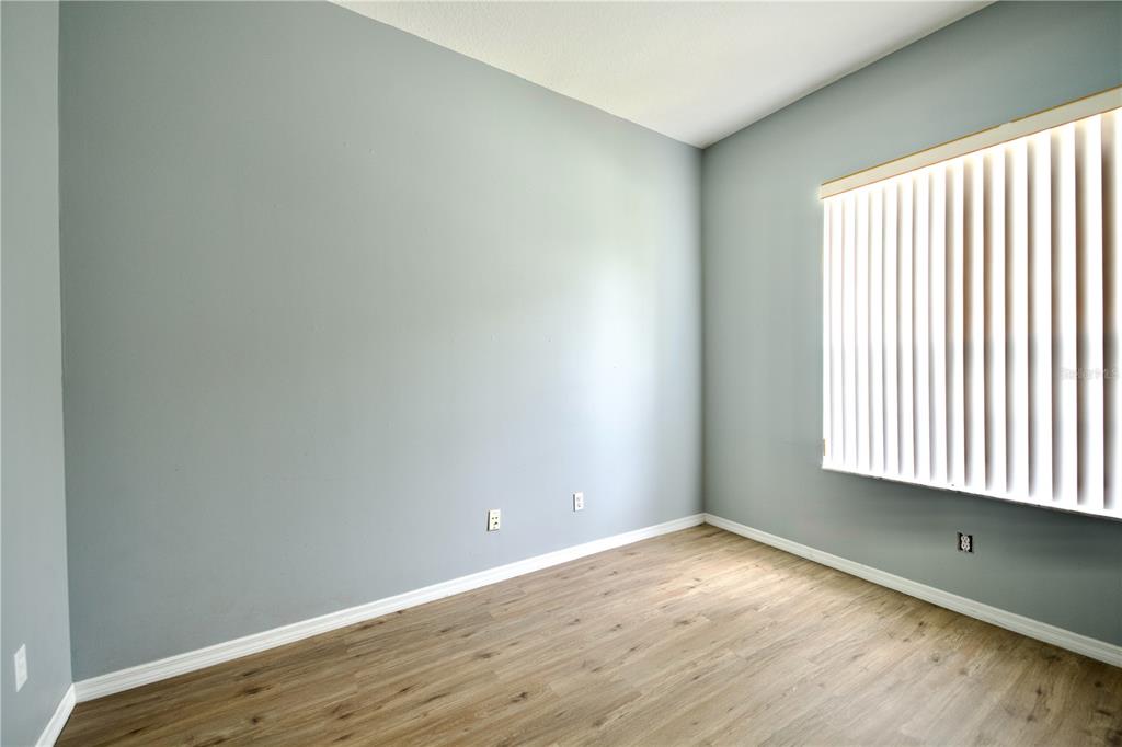 An empty room features light gray walls, wood-look flooring, and a window with vertical blinds — 13808 RUDI LOOP, SPRING HILL, FL