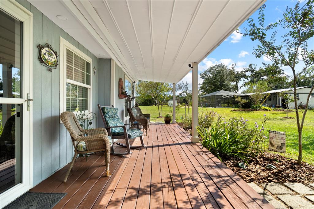 A covered wooden porch features wicker rocking chairs alongside a blue-sided house and yard — 7650 NE 40TH STREET, HIGH SPRINGS, FL