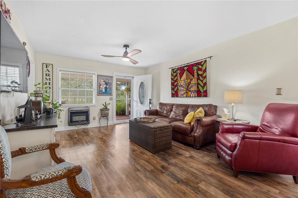 A living room features wood-look flooring, a brown leather sofa, a red armchair, and a ceiling fan — 7650 NE 40TH STREET, HIGH SPRINGS, FL