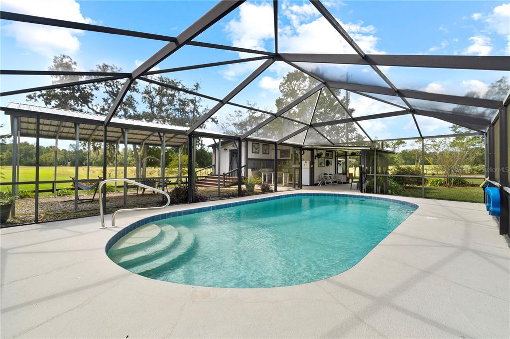 A screened-in swimming pool with concrete decking overlooks a grassy field and a small building — 7650 NE 40TH STREET, HIGH SPRINGS, FL