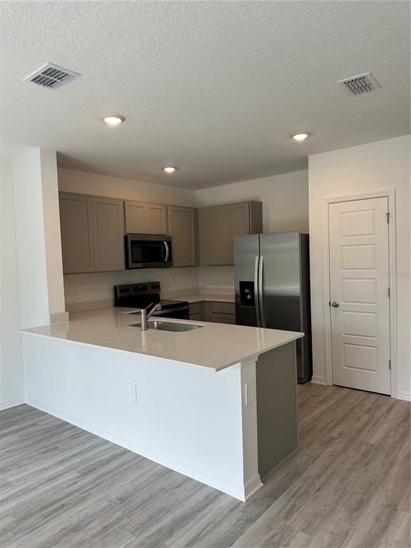 A modern kitchen features gray cabinets, stainless steel appliances, and a white quartz island countertop — 1823 ROCK ELM ROAD, DAVENPORT, FL