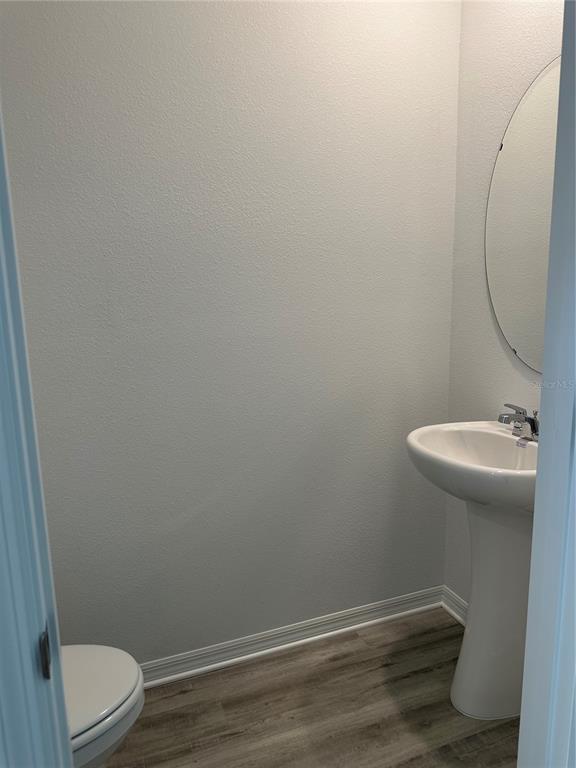 A small bathroom features a pedestal sink, an oval mirror, and light wood-look flooring — 1823 ROCK ELM ROAD, DAVENPORT, FL