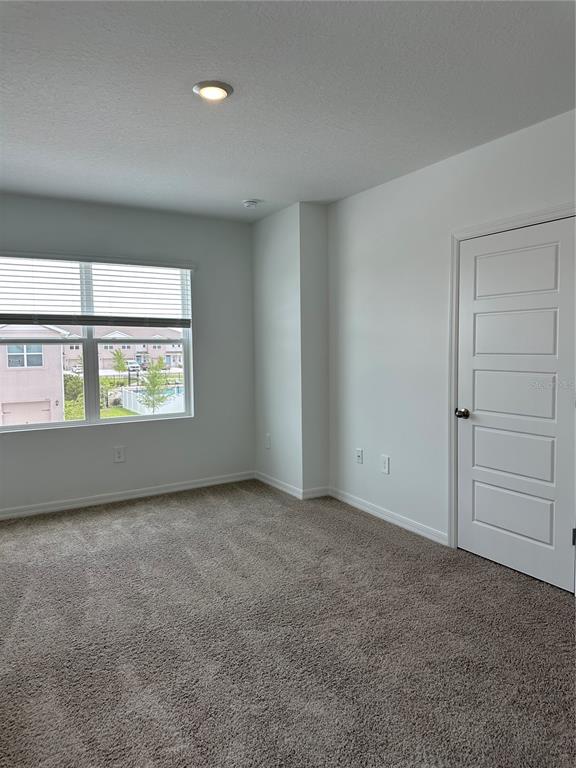 An empty bedroom features beige carpet, white walls, a window with blinds, and a door — 1823 ROCK ELM ROAD, DAVENPORT, FL