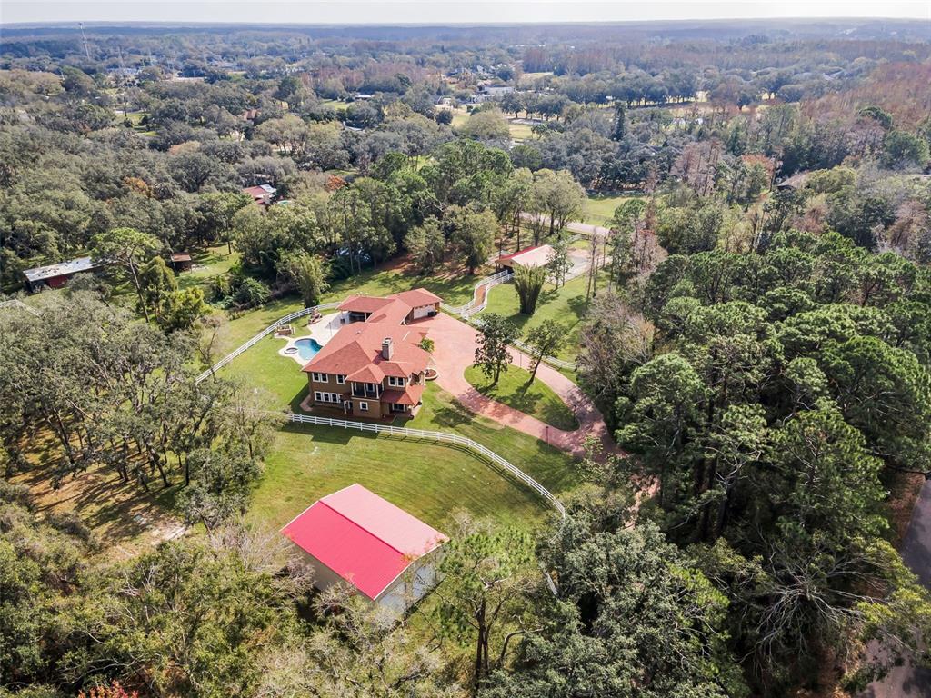 An aerial view shows a house with a red roof, pool, and outbuildings amidst trees — 249 DOGWOOD TRACE, TARPON SPRINGS, FL