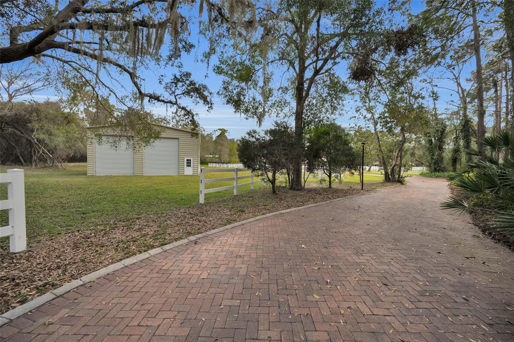 A brick driveway leads toward a detached two-car garage on a grassy, tree-lined property — 249 DOGWOOD TRACE, TARPON SPRINGS, FL