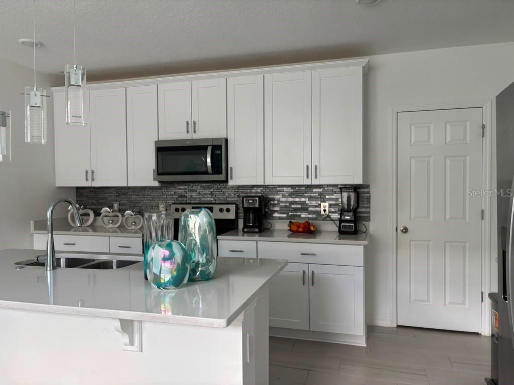 A kitchen with white cabinets, a kitchen island, stainless steel appliances, and a tiled backsplash — 1446 SEA GLASS ROAD, HAINES CITY, FL