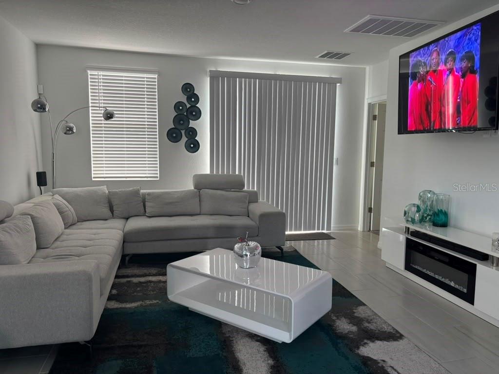 A modern living room features a gray sectional sofa, white coffee table, and wall-mounted television — 1446 SEA GLASS ROAD, HAINES CITY, FL