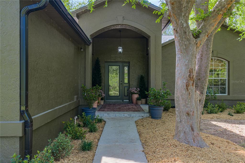 A concrete walkway leads to the arched entryway of a green stucco house — 9091 MCINTYRE ROAD, BROOKSVILLE, FL