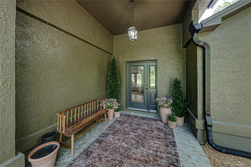 A covered entryway features a wooden bench, a patterned rug, and potted plants by the door — 9091 MCINTYRE ROAD, BROOKSVILLE, FL