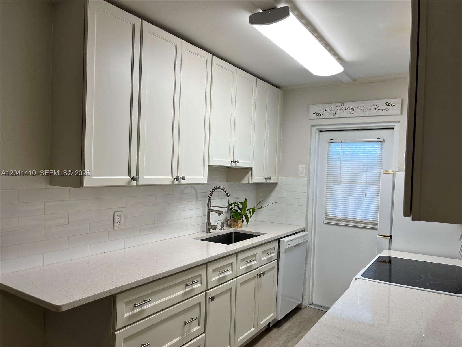 A kitchen features white cabinets, light countertops, a subway tile backsplash, and a white door — 6550 Royal Palm Blvd # 105A, Margate FL 33063, MARGATE, FL