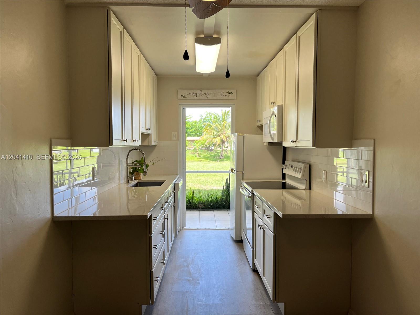 A galley kitchen features white cabinets, light countertops, a subway tile backsplash, and a glass door — 6550 Royal Palm Blvd # 105A, Margate FL 33063, MARGATE, FL