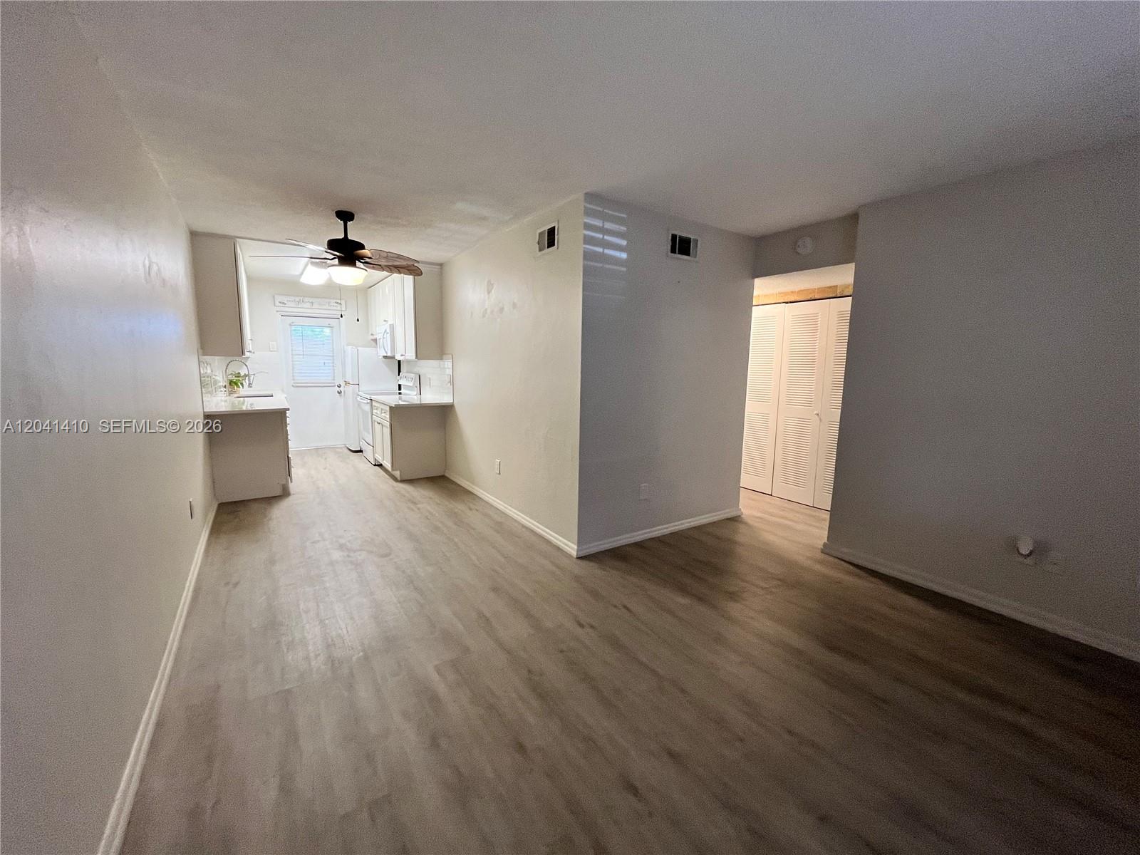 An open-concept room features light wood-look flooring, white walls, and an adjacent kitchen area — 6550 Royal Palm Blvd # 105A, Margate FL 33063, MARGATE, FL