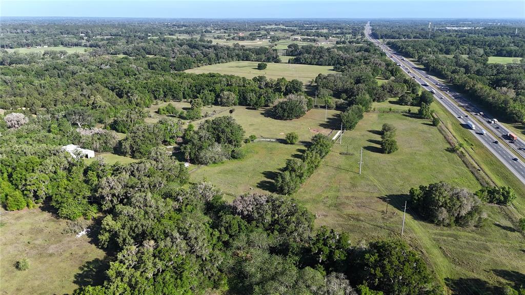 An aerial view shows a large, grassy property with scattered trees adjacent to a highway — 9126 NW 49TH AVENUE ROAD, OCALA, FL