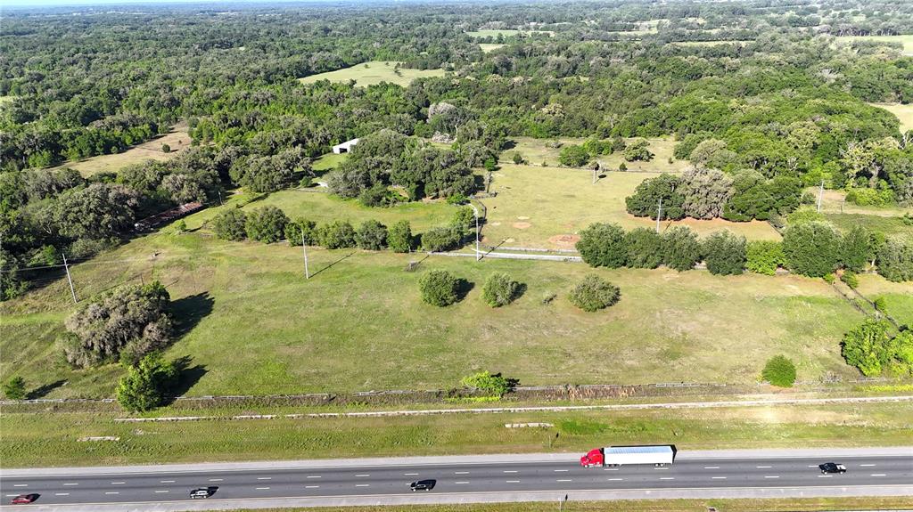 An aerial view shows a large, grassy field bordered by trees and a multi-lane highway — 9126 NW 49TH AVENUE ROAD, OCALA, FL
