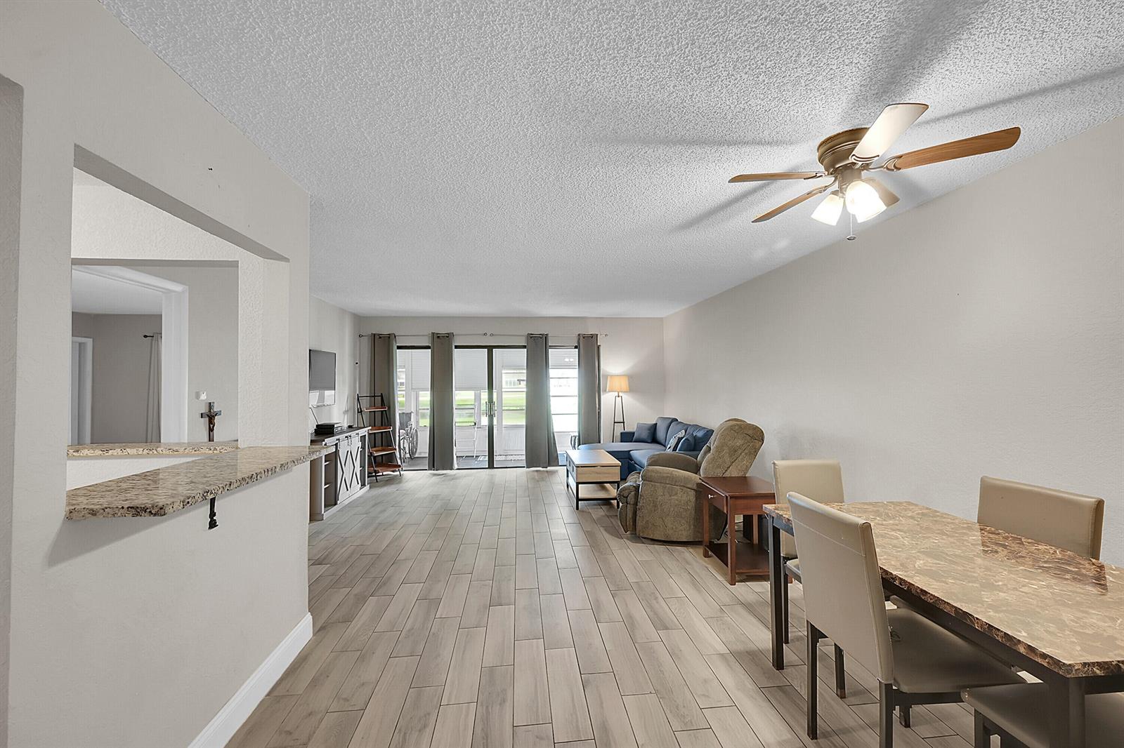 A living and dining area with light wood-look tile floors, a ceiling fan, and sliding doors — 497 Piedmont K, Delray Beach FL 33484, DELRAY BEACH, FL