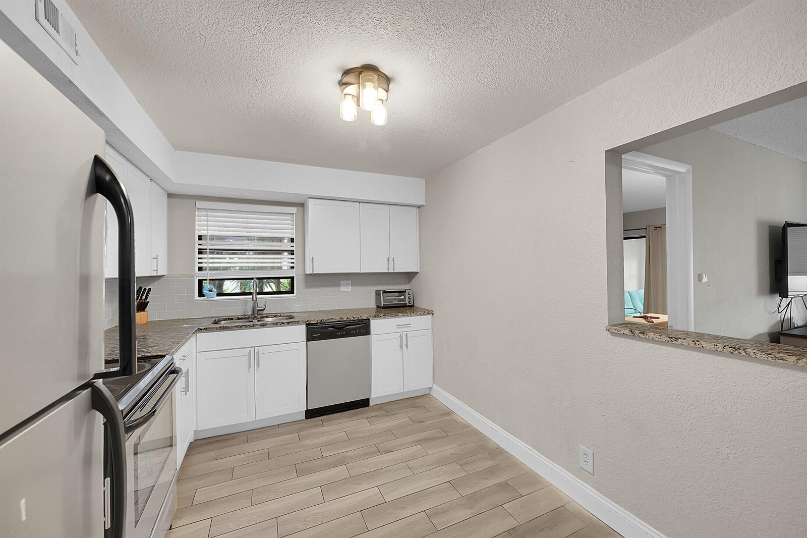 A kitchen with white cabinets, stainless steel appliances, granite countertops, and light wood-look tile flooring — 497 Piedmont K, Delray Beach FL 33484, DELRAY BEACH, FL