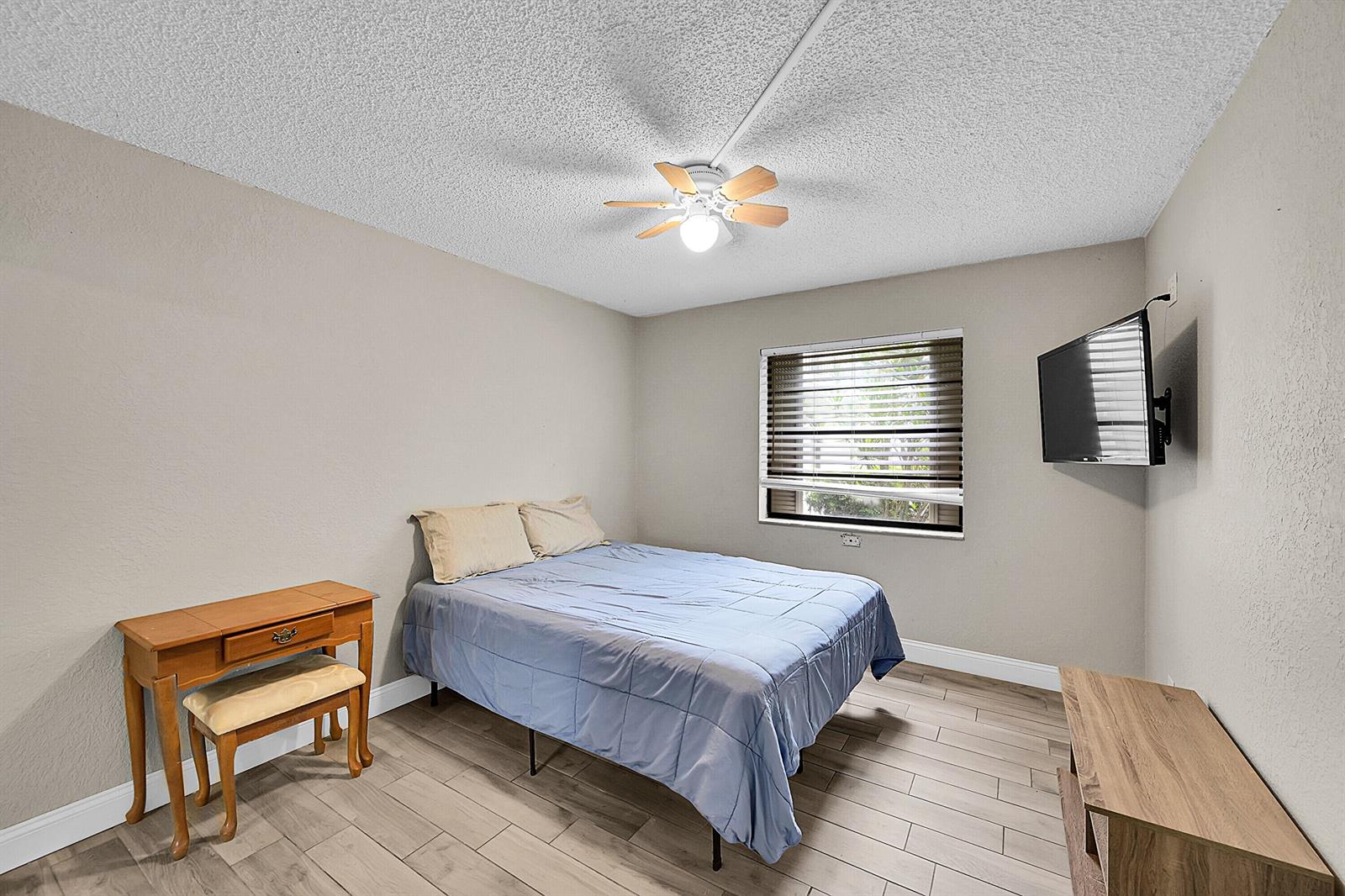A bedroom with light gray walls, wood-look tile flooring, a ceiling fan, and a wall-mounted television — 497 Piedmont K, Delray Beach FL 33484, DELRAY BEACH, FL