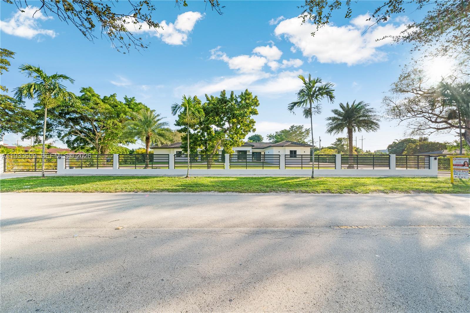 A single-story house sits behind a long white wall with black metal fencing and palm trees — 10398 SW 64th St, Miami FL 33173, MIAMI, FL