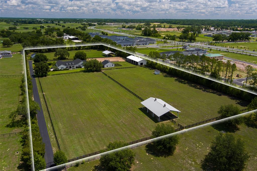 An aerial view of a fenced property featuring a house, barns, and open pasture land — 4985 SW 85TH STREET, OCALA, FL