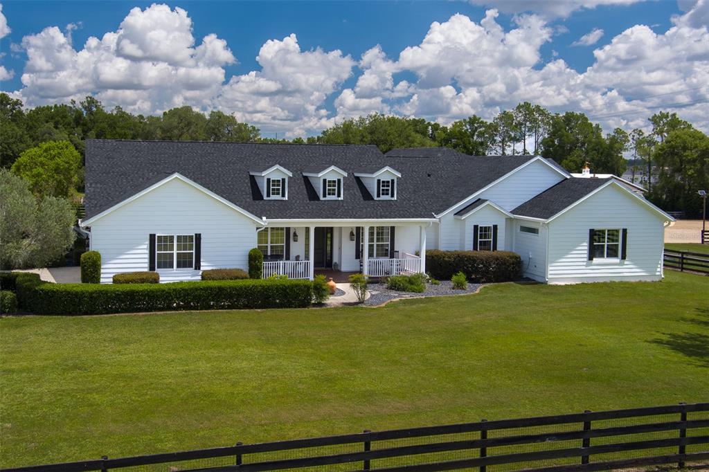 A white farmhouse with a dark shingled roof and black shutters sits behind a fence — 4985 SW 85TH STREET, OCALA, FL