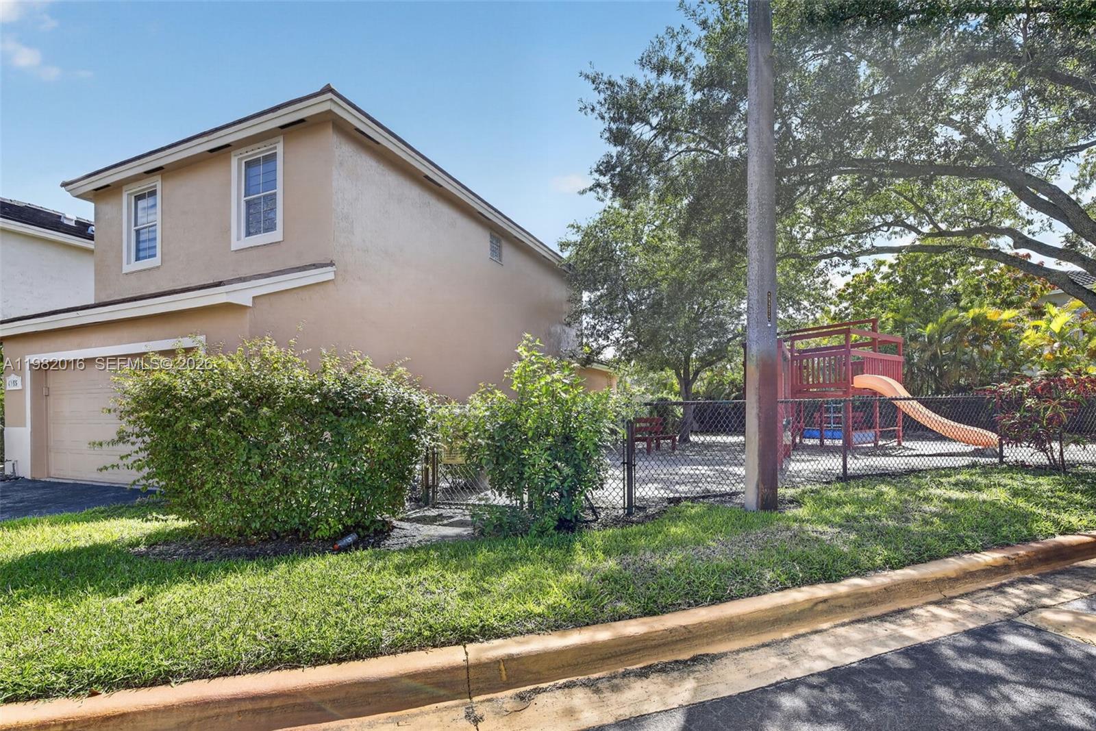 A two-story house exterior features a garage, a fenced side yard, and a playground set — 6955 SW 148th Ln, Davie FL 33331, DAVIE, FL