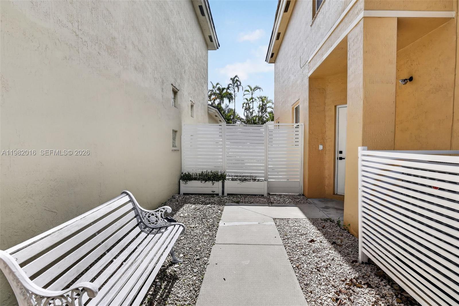 A white bench sits on a gravel path between two stucco building walls — 6955 SW 148th Ln, Davie FL 33331, DAVIE, FL