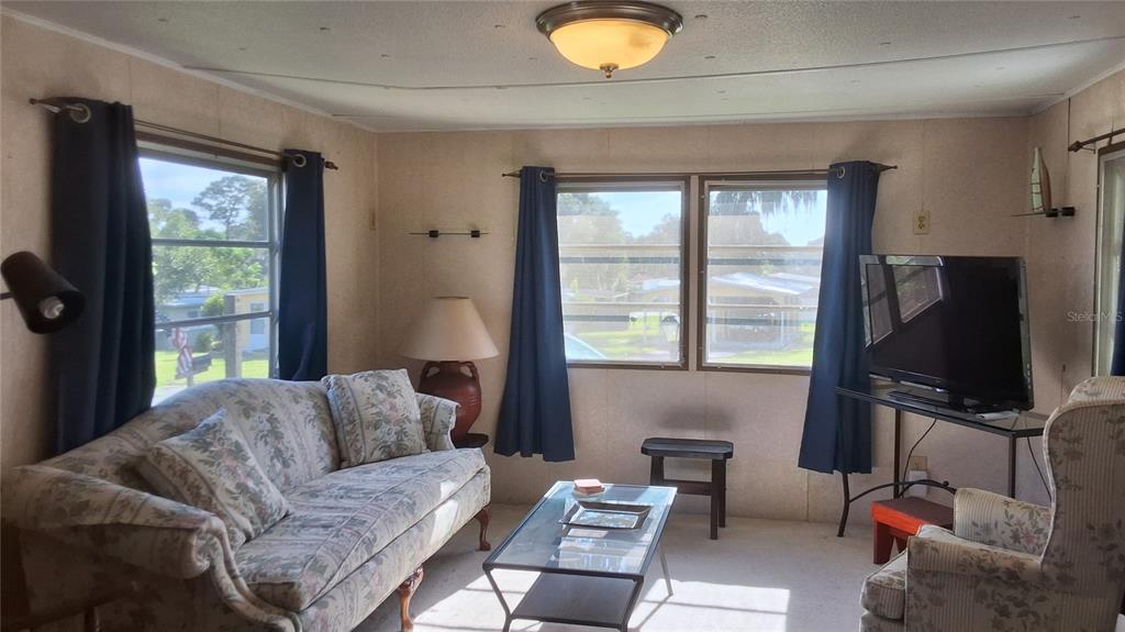 A living room features a floral sofa, a glass coffee table, and windows with blue curtains — 2488 N PARK POINT, HERNANDO, FL