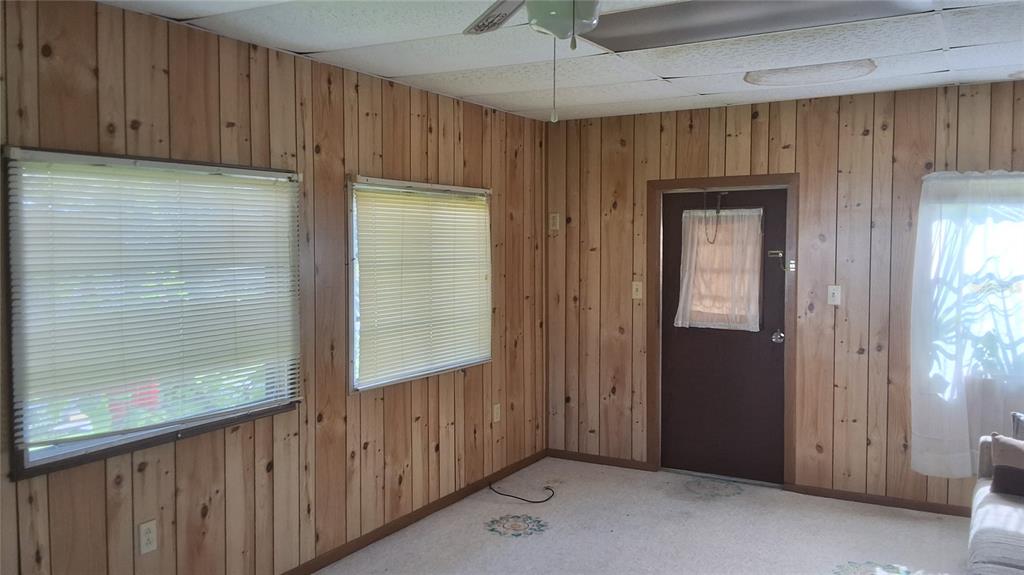A room with wood-paneled walls, two windows with blinds, a door, and a ceiling fan — 2488 N PARK POINT, HERNANDO, FL
