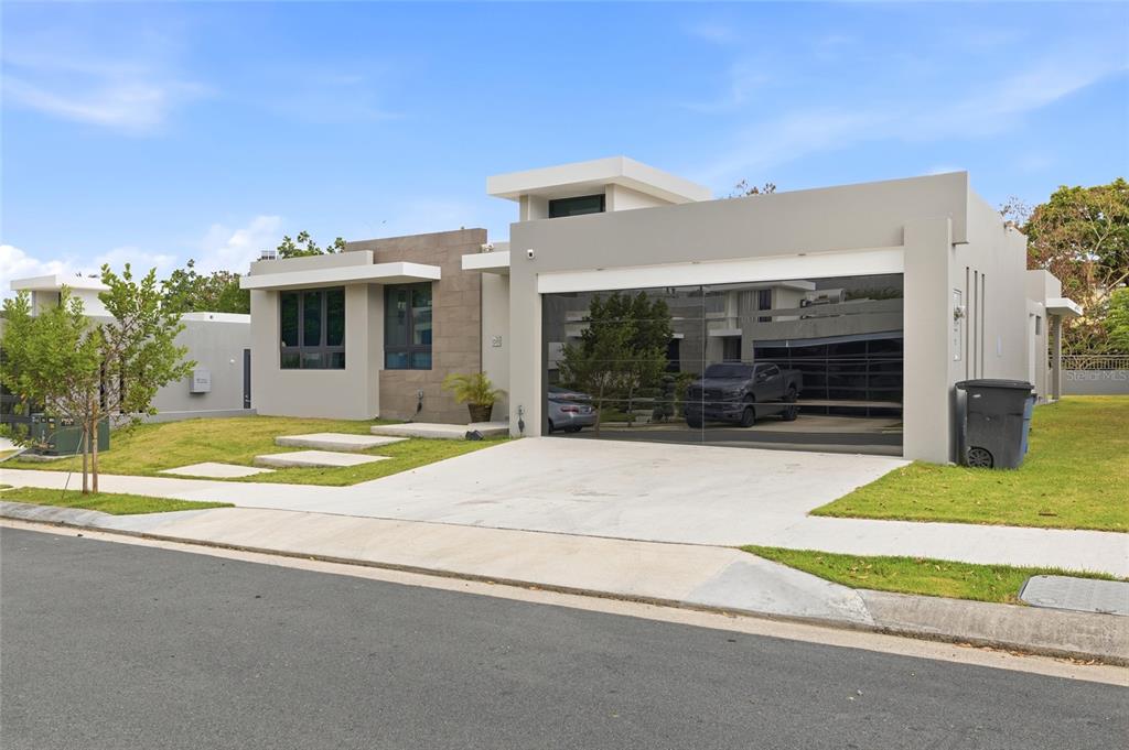 A modern single-story house with a concrete driveway, a mirrored garage door, and stone accents — Urb Las Casonas ARANDA, GUAYNABO, PR