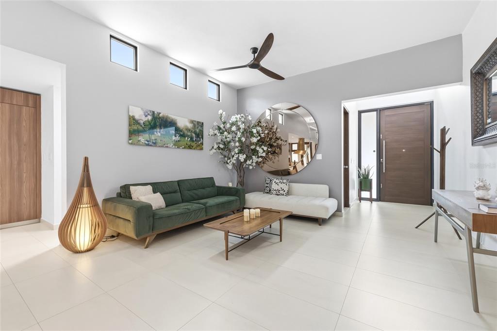 A modern living room features a green sofa, white bench, round mirror, and tile flooring — Urb Las Casonas ARANDA, GUAYNABO, PR