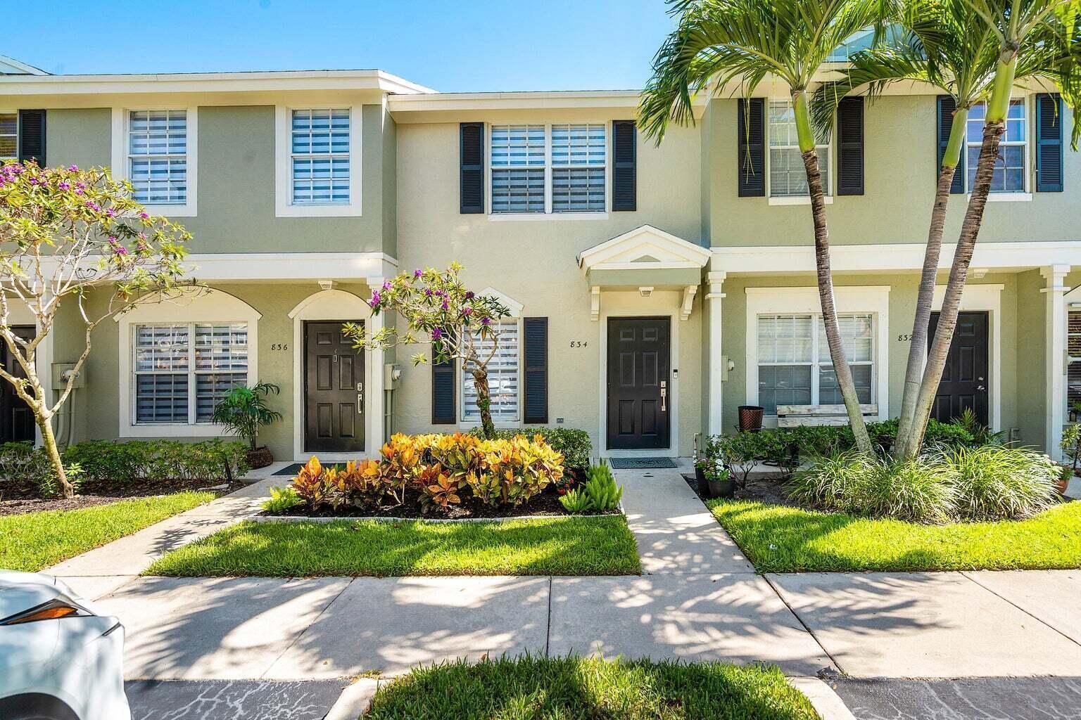 A row of three attached townhouses with light green siding, dark doors, and front landscaping — 834 Kokomo Key Lane, Delray Beach FL 33483, DELRAY BEACH, FL