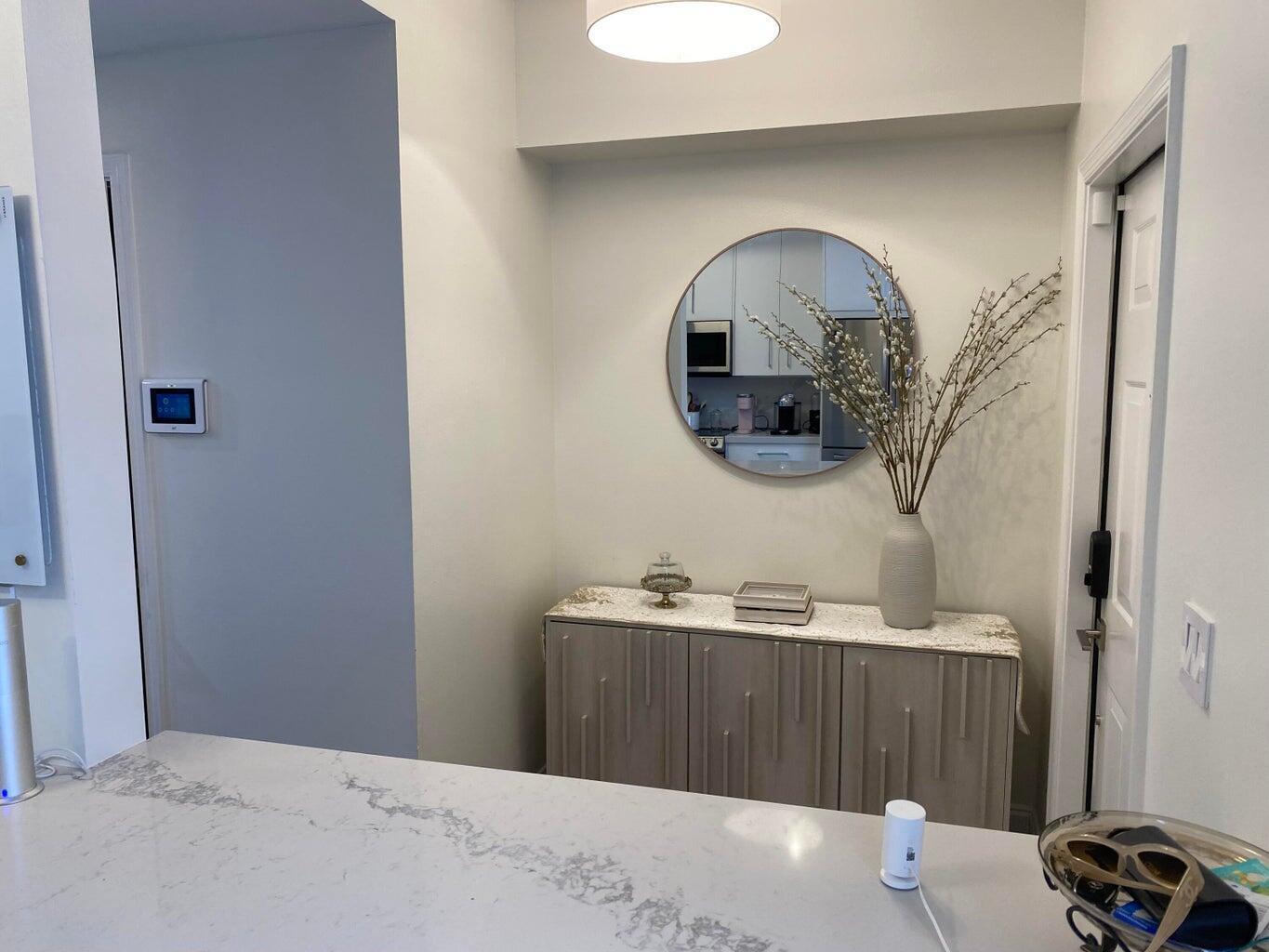 A console table with a mirror and vase sits in a hallway near a kitchen — 834 Kokomo Key Lane, Delray Beach FL 33483, DELRAY BEACH, FL