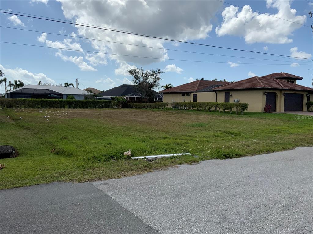 A vacant, grassy residential lot sits between two existing houses under a cloudy sky — 2510 MIRACLE PARKWAY, CAPE CORAL, FL