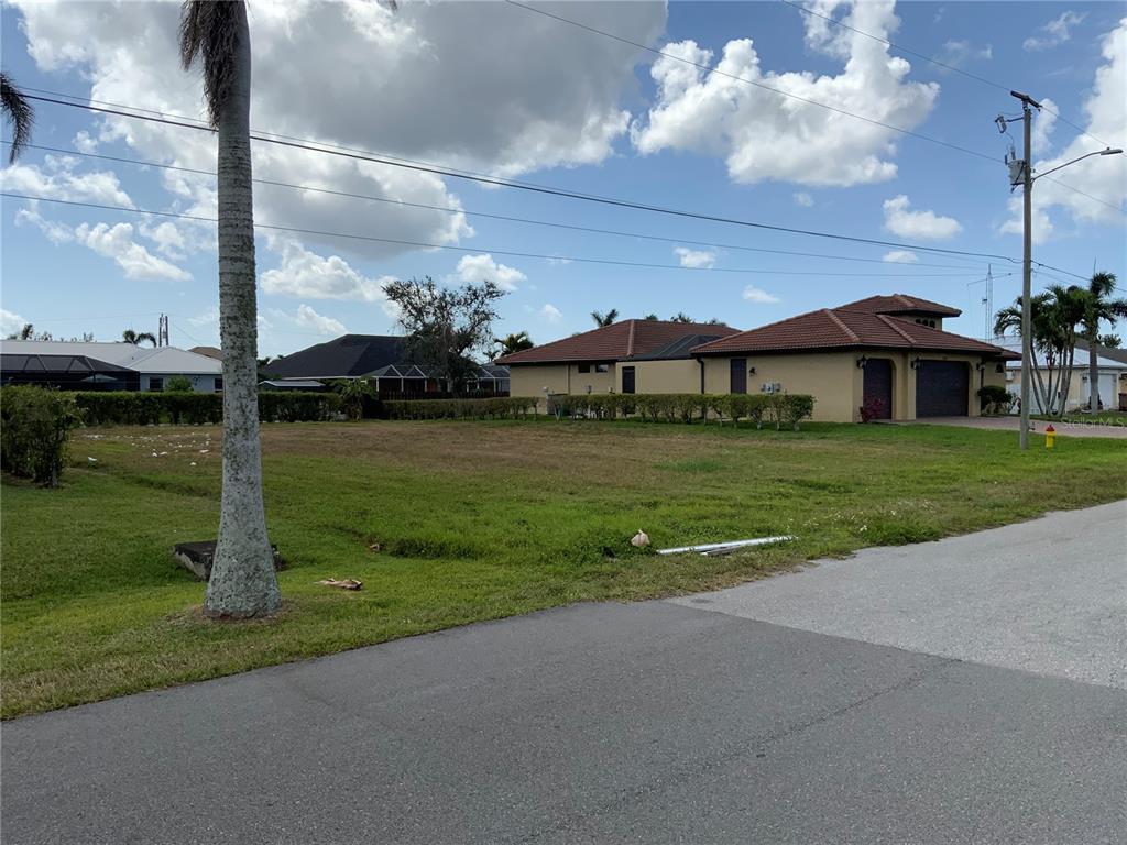 A vacant grassy lot sits between two residential houses under a partly cloudy sky — 2510 MIRACLE PARKWAY, CAPE CORAL, FL