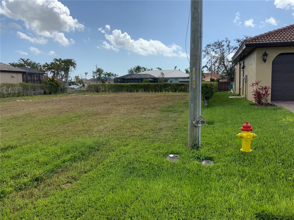 A vacant grassy lot sits next to a house with a fire hydrant and utility pole — 2510 MIRACLE PARKWAY, CAPE CORAL, FL