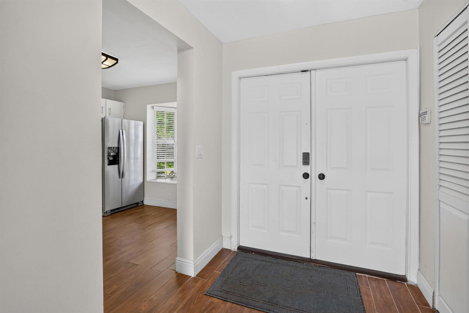 An entryway with wood-look flooring leads to a kitchen featuring a stainless steel refrigerator — 12175 NW 36th Place, Sunrise FL 33323, SUNRISE, FL