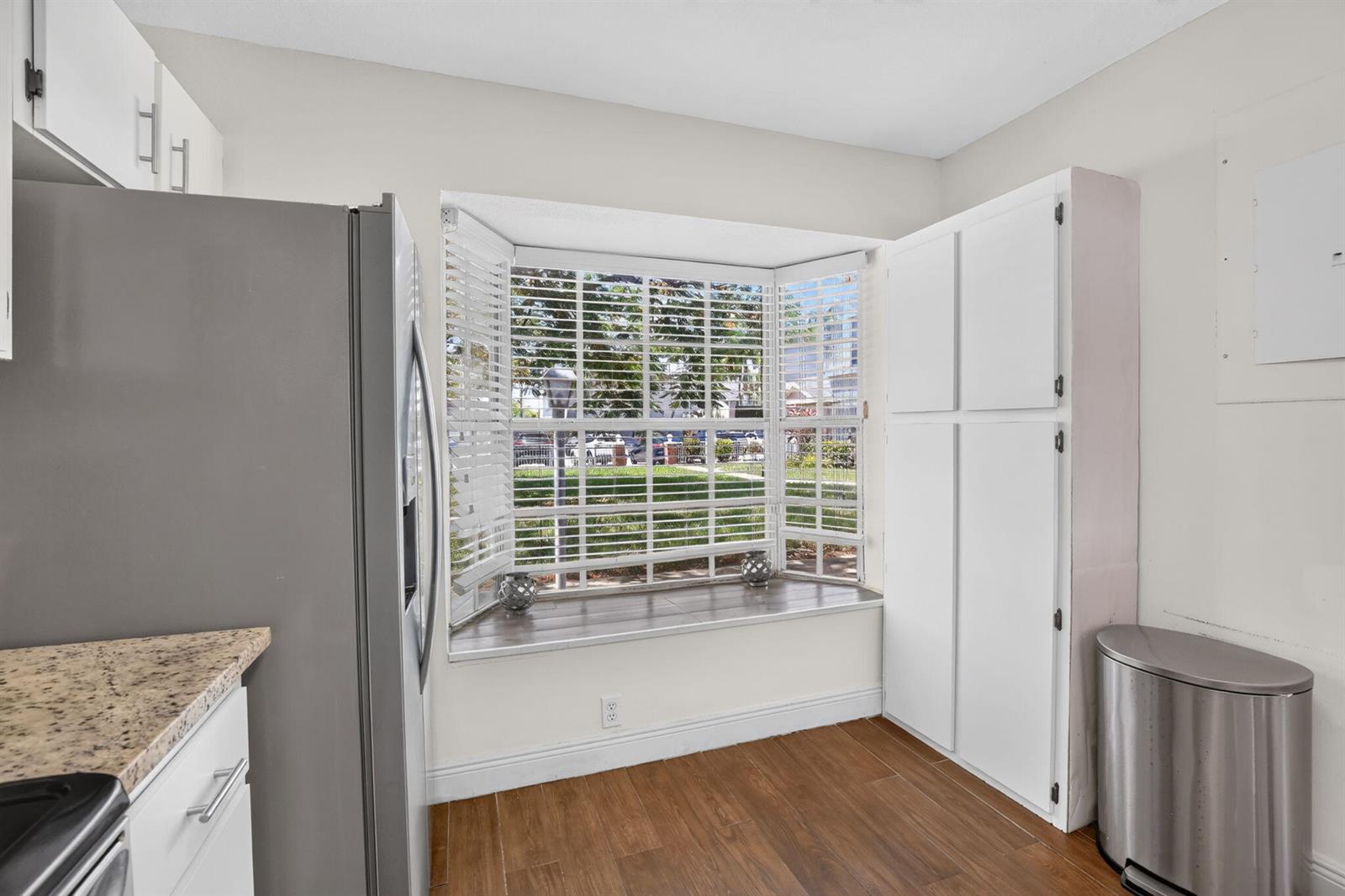 A kitchen features a bay window with blinds, white cabinetry, a gray refrigerator, and wood-look flooring — 12175 NW 36th Place, Sunrise FL 33323, SUNRISE, FL