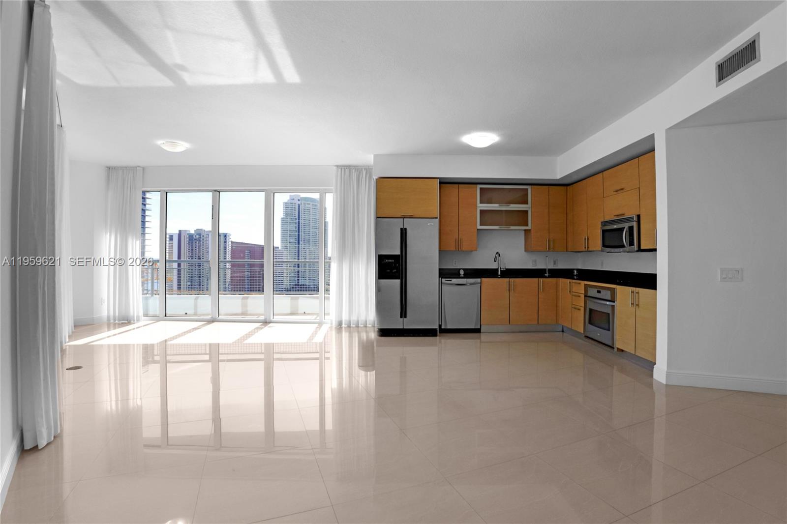 A modern kitchen with light wood cabinets and stainless steel appliances opens to a living area — 60 SW 13th St # 1700, Miami FL 33130, MIAMI, FL