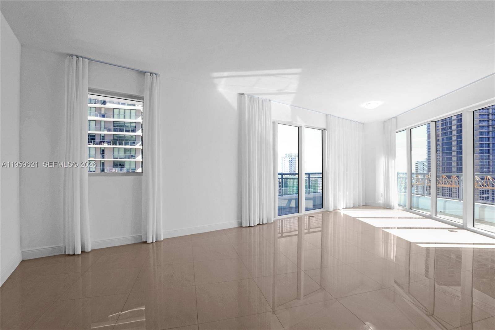 A bright, empty room features large windows, white walls, and glossy beige tile flooring — 60 SW 13th St # 1700, Miami FL 33130, MIAMI, FL