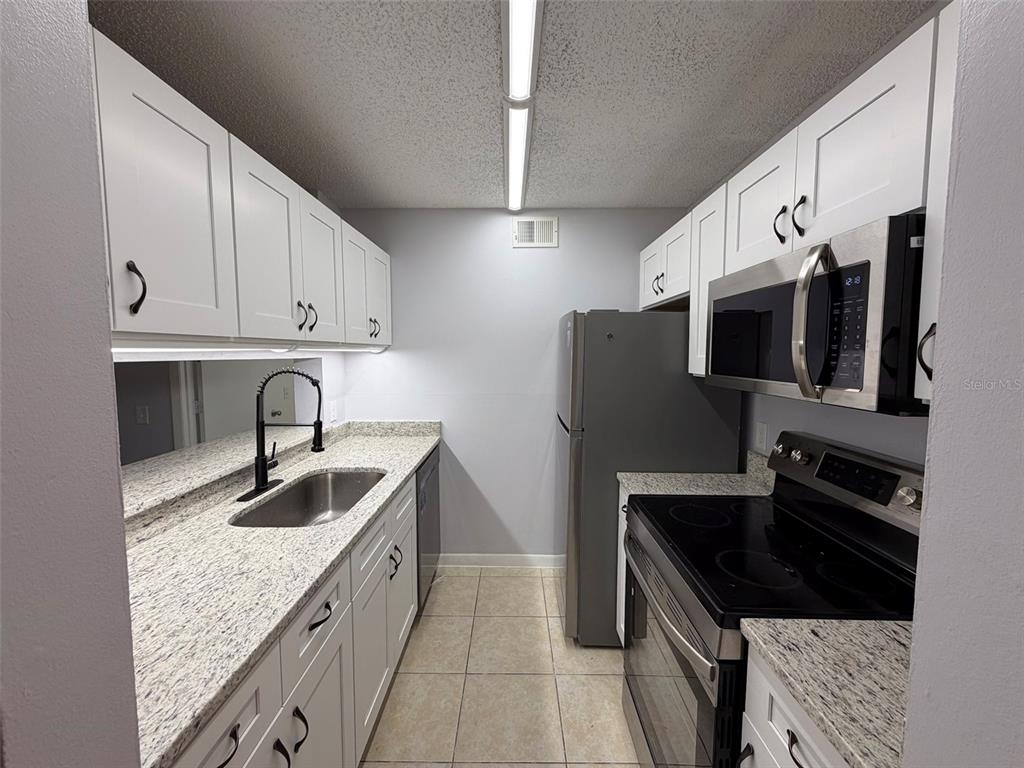 A galley kitchen features white cabinets, granite countertops, stainless steel appliances, and tile flooring — 3921 SW 34TH STREET UNIT 301, GAINESVILLE, FL