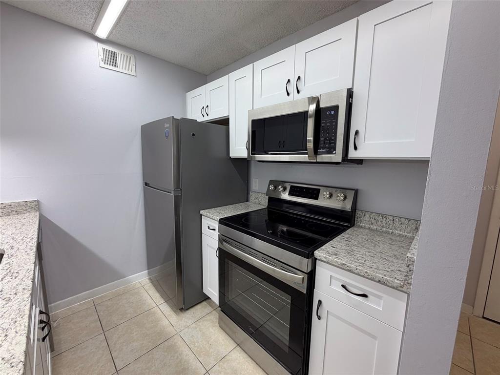 A kitchen features white cabinets, stainless steel appliances, and speckled granite countertops — 3921 SW 34TH STREET UNIT 301, GAINESVILLE, FL