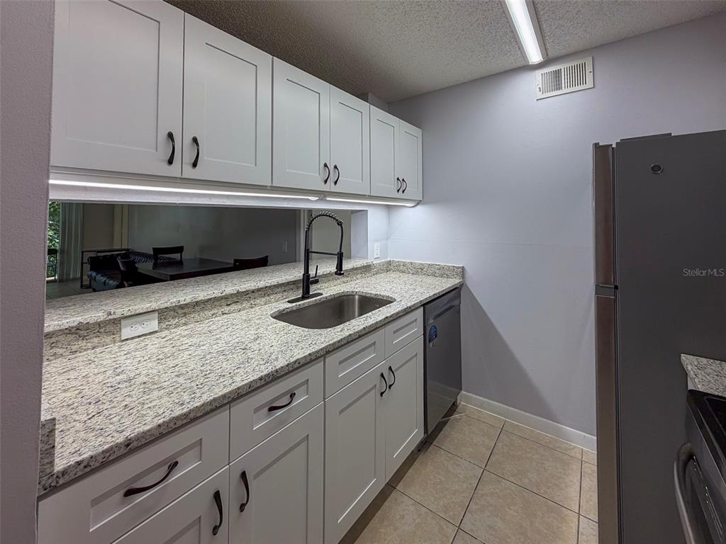 A kitchen features white cabinets, granite countertops, a stainless steel sink, and a gray refrigerator — 3921 SW 34TH STREET UNIT 301, GAINESVILLE, FL