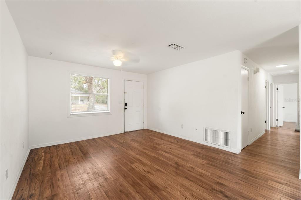 An empty living room features white walls, wood-look flooring, a ceiling fan, and a front door — 1911 SE 14TH AVENUE, GAINESVILLE, FL