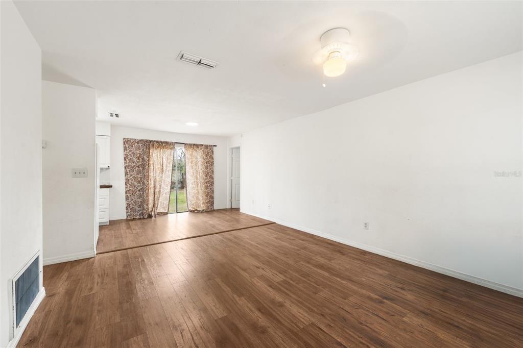 An empty living room features wood-look flooring, white walls, and a sliding glass door — 1911 SE 14TH AVENUE, GAINESVILLE, FL
