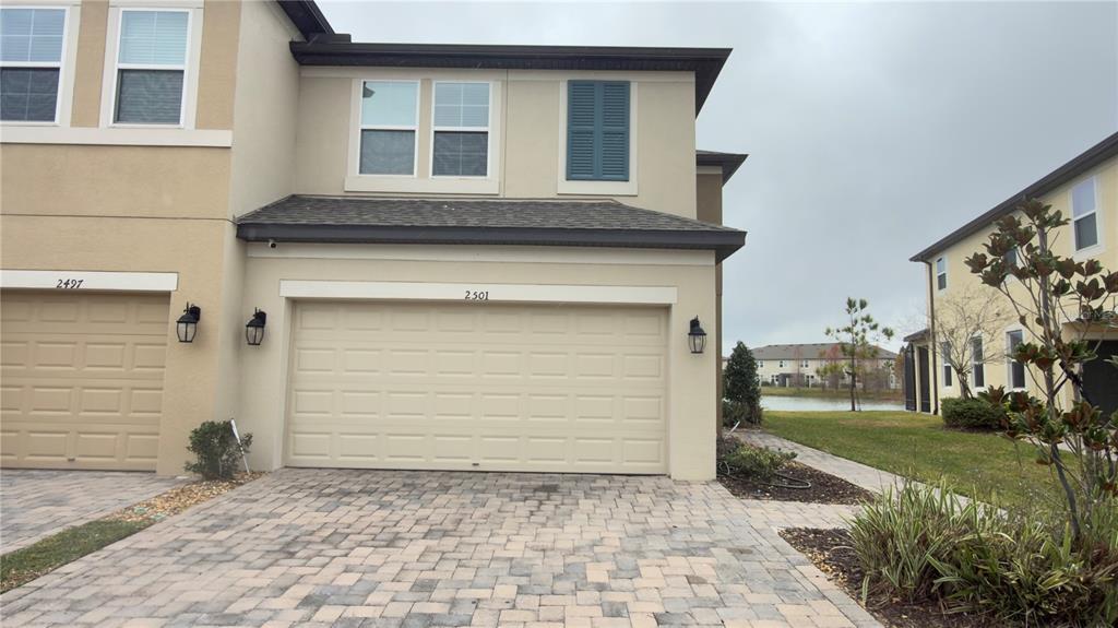 The exterior of a two-story townhouse features a beige stucco facade and a two-car garage — 2501 STAPLEFORD PLACE, WESLEY CHAPEL, FL