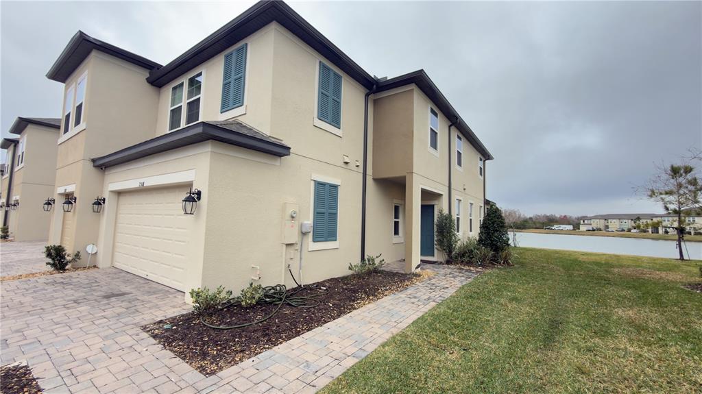A two-story tan stucco townhouse with a garage, blue shutters, and a paved walkway — 2501 STAPLEFORD PLACE, WESLEY CHAPEL, FL